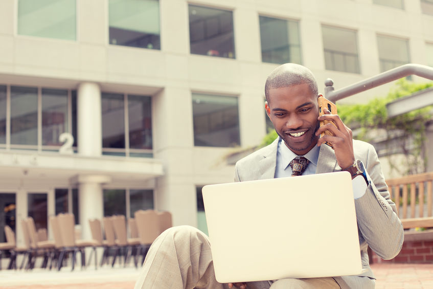 Businessman working with laptop outdoors talking on mobile phone