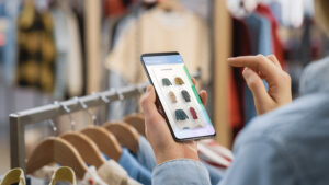 clothing store: female using smartphone with online fashion store user interface to chek prices on a stylish branded items. close up over the shoulder shot of a mobile device.